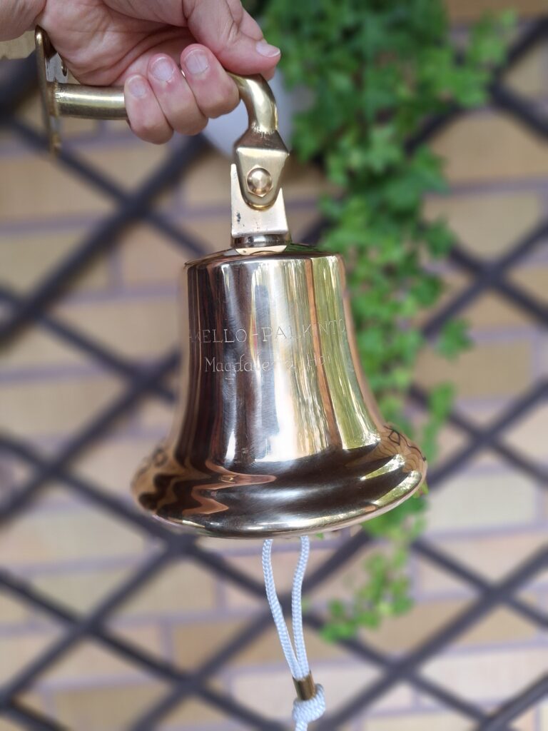 Kuvassa Laivakello-palkinto, joka on laivakello, vasten tiiliseinää ja murattia.