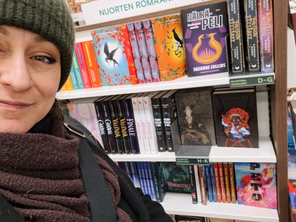 Kirjailija Hai talvitamineissaan Akateemisen kirjakaupun nuortenkirjahyllyllä, jossa vierekkäin Sarvijumala ja Kuunkehä.